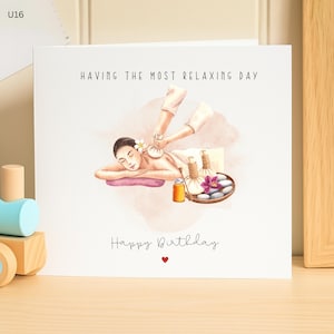 Op de afbeelding: Een witte wenskaart met een aquarel illustratie van een persoon die een massage krijgt. De kaart leest "HAVING THE MOST RELAXING DAY" en "Happy Birthday" met een rood hart. Een houten speelgoedtrein staat in de linker benedenhoek.
