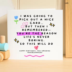 May include: A white birthday card with the message: "I WAS GOING TO PICK OUT A NICE CARD... BUT THEN I REMEMBERED - YOU'RE THE REASON LIFE'S NEVER BORING. SO THIS WILL DO." Decorated with a blue flower, pink shapes, and a pink heart.