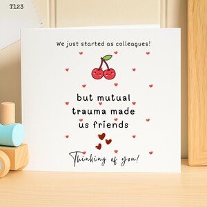 Op de afbeelding: Een witte wenskaart met de tekst "We just started as colleagues! but mutual trauma made us friends Thinking of you!" en een illustratie van kersen. Kleine rode hartjes zijn verspreid rond de tekst en de afbeelding.