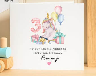 May include: A white birthday greeting card featuring a watercolor illustration of a unicorn, balloons, and gifts next to a large number 3. The text reads: TO OUR LOVELY PRINCESS HAPPY 3RD BIRTHDAY Emmy, followed by a small pink heart.