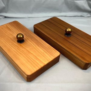May include: Two rectangular wooden boxes with brass knobs. One box is light-colored, the other is dark. The boxes are made of wood and have a simple, elegant design. The knobs are small and round.