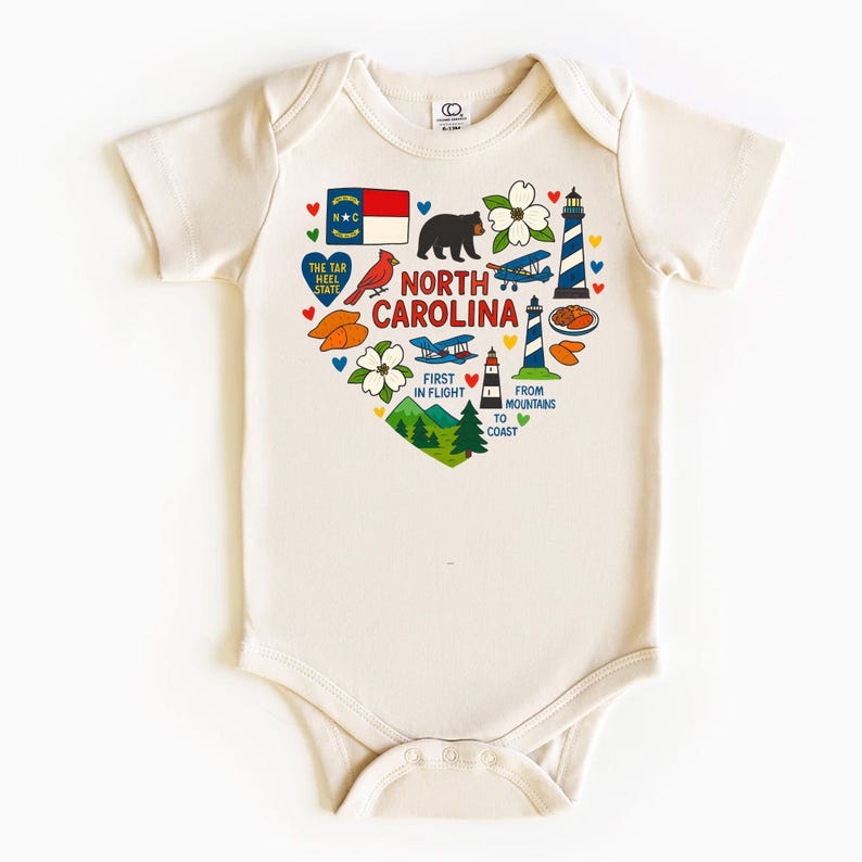 May include: Cream-colored baby bodysuit with a heart-shaped graphic featuring North Carolina state symbols. The design includes a flag, bear, flowers, lighthouse, and text that reads "North Carolina" and "First in Flight."