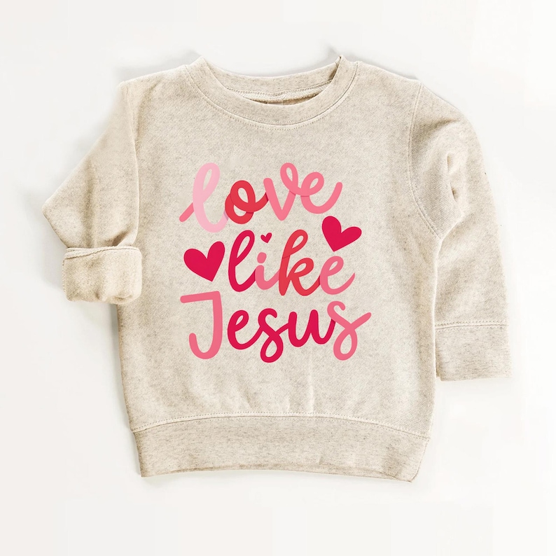 Peut inclure: Un sweat-shirt beige avec le texte "love like Jesus" en lettres roses et rouges avec des c&oelig;urs.