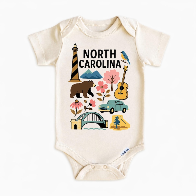 May include: Cream-colored baby bodysuit with a colorful graphic of North Carolina landmarks, including a lighthouse, mountains, bear, guitar, car, and bridge. The words "North Carolina" are printed in black.