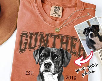 May include: A terracotta-colored t-shirt featuring a graphic of a black and white dog, the name GUNTHER in dark brown block letters, and the text EST. 2019. The shirt includes a Comfort Colors label and a small inset photo of a dog.