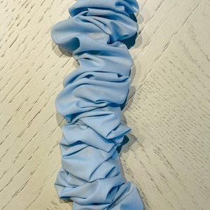 Könnte beinhalten: Ein langer Streifen aus hellblauem Stoff, der zu Rüschen gerafft ist. Der Stoff ist weich und fließend und erzeugt einen zarten und eleganten Look.