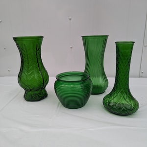 May include: Four green glass vases of different shapes and sizes. The vases are all made of textured glass and have a vintage look.