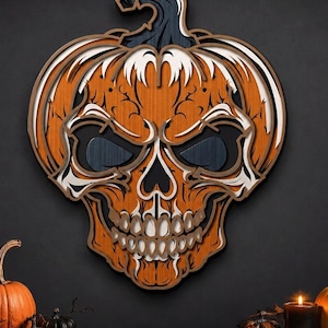 May include: A layered wooden wall art piece shaped like a pumpkin with a skull face. The design features orange, white, and dark blue wood tones with intricate cutouts forming the eyes, nose, and teeth. The pumpkin stem is dark blue.