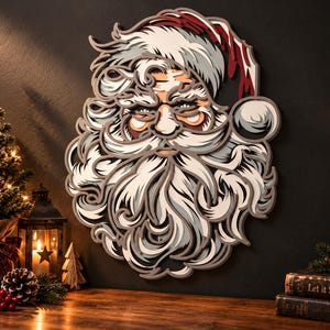 Può includere: Un'opera d'arte da parete in legno a più strati che raffigura il volto di Babbo Natale con barba, baffi e cappello dettagliati. Il design presenta ritagli sovrapposti in tonalità di bianco, grigio e rosso, creando un effetto tridimensionale.