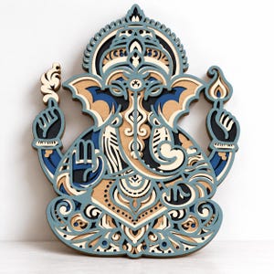 May include: A multi-layered wooden wall art piece depicting the deity Ganesha. The design features intricate cutouts in shades of light blue, dark blue, black, and natural wood tones, creating a dimensional effect with detailed patterns.