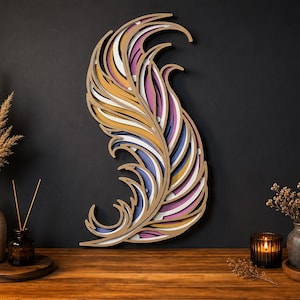 May include: A multi-layered wooden wall art piece shaped like a curved feather, featuring stacked cutouts in shades of mustard yellow, soft pink, deep purple, and white, creating a dimensional effect with visible depth between the layers.