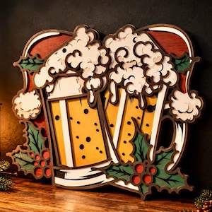 May include: A layered wooden wall art piece featuring two beer mugs filled with yellow liquid and white foam. The design includes red background accents, green holly leaves, and red berries. The artwork has a multi-dimensional, cutout aesthetic.