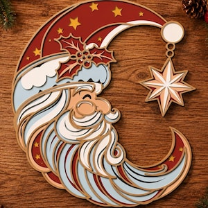 Op de afbeelding: Een gelaagde houten wanddecoratie in de vorm van een halve maan met een kerstmangezicht met een lange witte baard, een rode muts met gele sterren en een hulsttakje. Een achtpuntige ster hangt aan de punt van de maan.