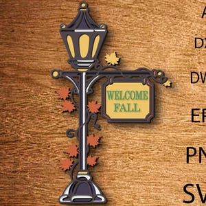 Könnte beinhalten: Eine dekorative Laterne mit einem Schild mit der Aufschrift „WELCOME FALL“. Das Schild ist gelb mit grünem Text und von einem braunen Rahmen umgeben. Die Laterne ist schwarz und hat orangefarbene Blätter.