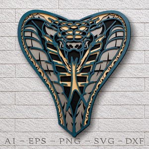 May include: A multi-layered wall art piece shaped like a cobra head, featuring intricate cutouts in shades of blue, beige, gray, and black. The design displays a stylized snake with a flared hood and a forked tongue, with text at the bottom reading AI-EPS-PNG-SVG-DXF.