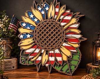 May include: A multi-layered wooden sunflower wall art piece featuring a central brown lattice disc surrounded by petals painted in yellow, red, white, and blue with white stars. The design incorporates American flag motifs and green leaves.