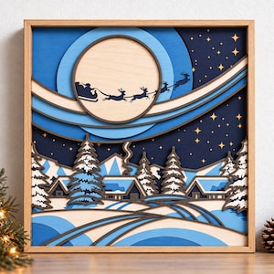 May include: A multi-layered wooden wall art piece in a light wood frame, depicting a winter night scene with a large moon, a silhouette of Santa and reindeer, snow-covered houses, pine trees, and a starry dark blue sky.