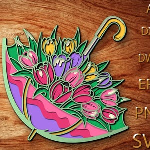 Puede incluir: Un diseño de arte en papel en capas de un paraguas colorido lleno de tulipanes. El paraguas es verde, rosa y morado, con un mango amarillo. Los tulipanes son rosas, amarillos y morados. El fondo es de madera.