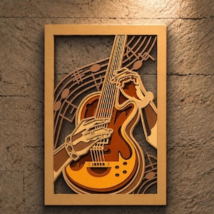 May include: A multi-layered wooden wall art piece featuring a guitar being played by hands, with musical notes and staff lines integrated into the design. The artwork uses various shades of brown and tan wood to create depth and dimension.