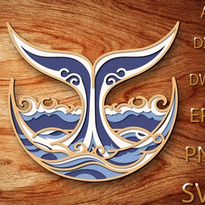 May include: A layered wooden art piece featuring a whale tail design with ocean waves. The artwork uses shades of blue, white, and tan, with the text "AI, DXF, DWG, EPS, PNG, SVG" in gold.