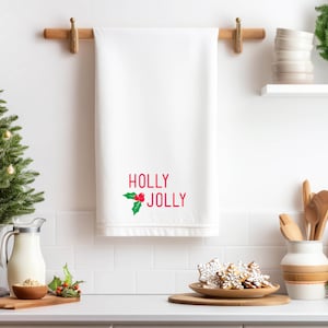 May include: White kitchen towel with red embroidery that says "HOLLY JOLLY" with a green holly sprig and red berries.