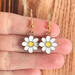 Small gold plated white daisy flower earrings dangling from gold earring hooks.