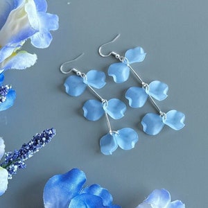 May include: A pair of dangle earrings with light blue flower petals hanging from silver hooks. The earrings are on a gray background.