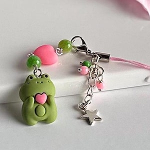 May include: A green frog charm with a pink heart, attached to a pink and green beaded phone strap with a silver star charm.