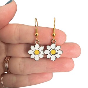 Small, dainty white daisy flower earrings with yellow centers, dangling from gold earring hooks.