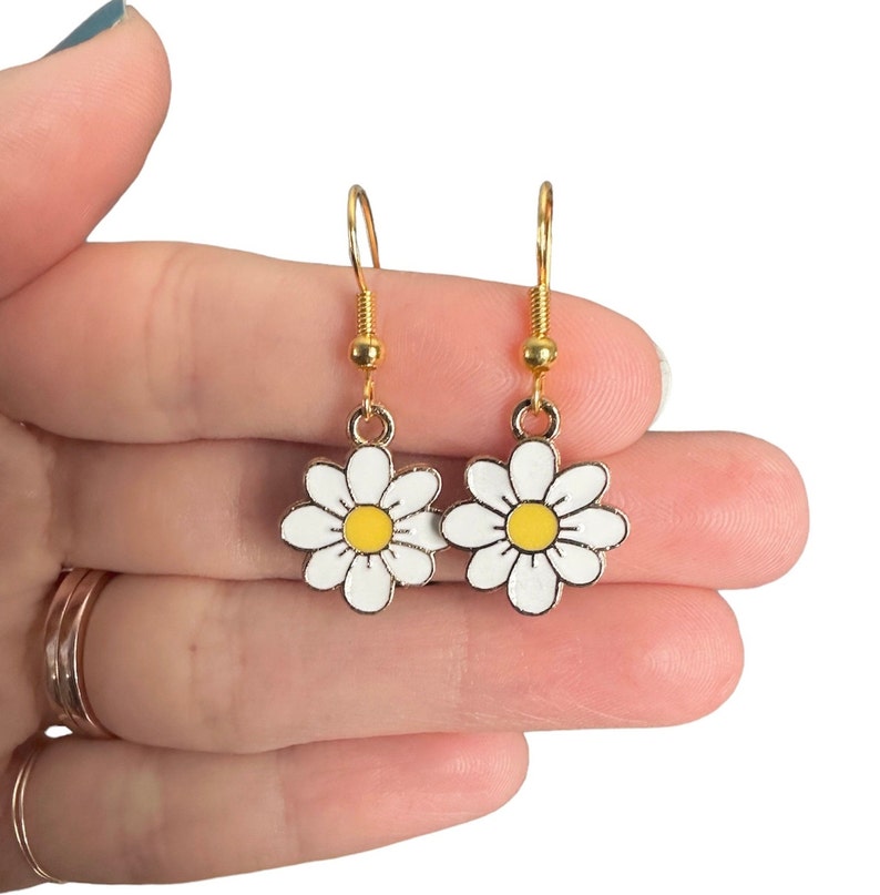 Small, dainty white daisy flower earrings with yellow centers, dangling from gold earring hooks.