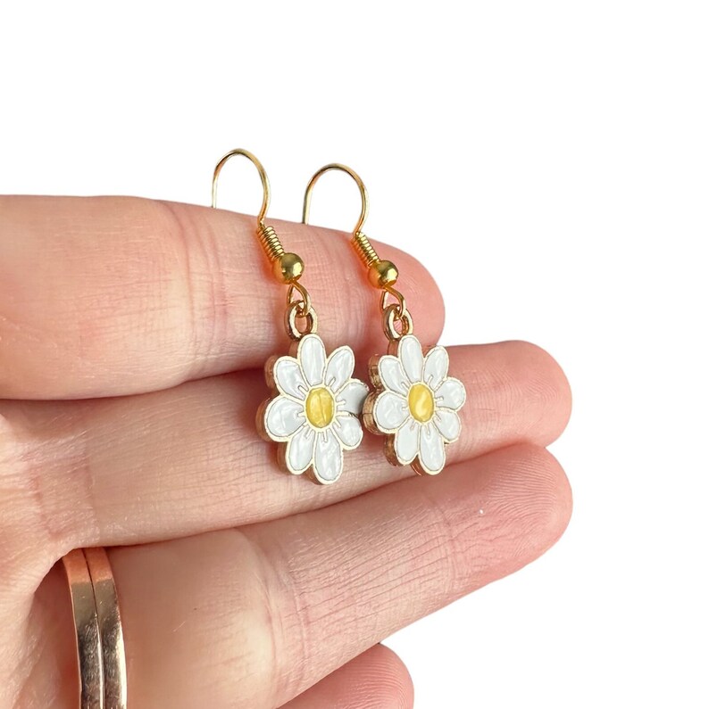 Small white daisy flower earrings with yellow centers, dangling from gold earring hooks.