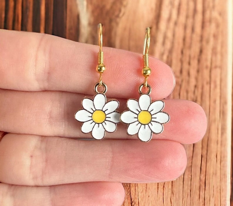 Small gold plated white daisy flower earrings dangling from gold earring hooks.