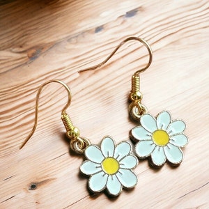 Small, dainty white daisy flower earrings with yellow centers, dangling from gold earring hooks.