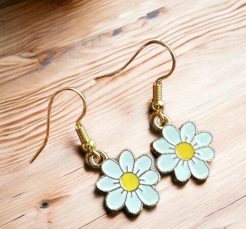 Small, dainty white daisy flower earrings with yellow centers, dangling from gold earring hooks.