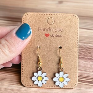 Small white daisy flower earrings with yellow centers, dangling from gold earring hooks, displayed on a Handmade with Love earring card.