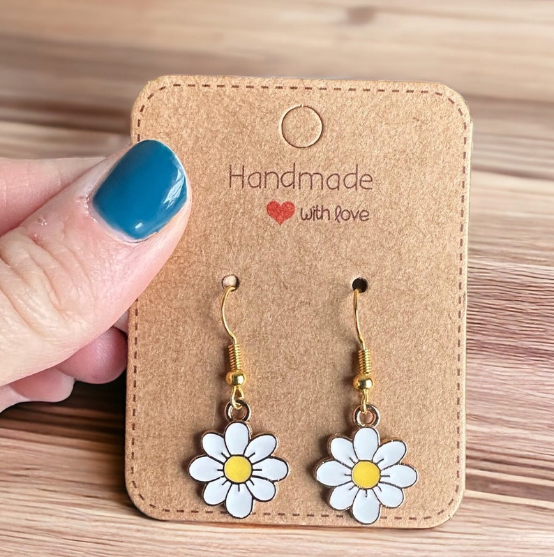 Small white daisy flower earrings with yellow centers, dangling from gold earring hooks, displayed on a Handmade with Love earring card.