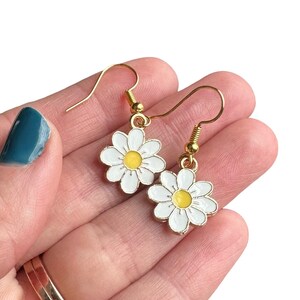 Small white daisy flower earrings with yellow centers, dangling from gold earring hooks.