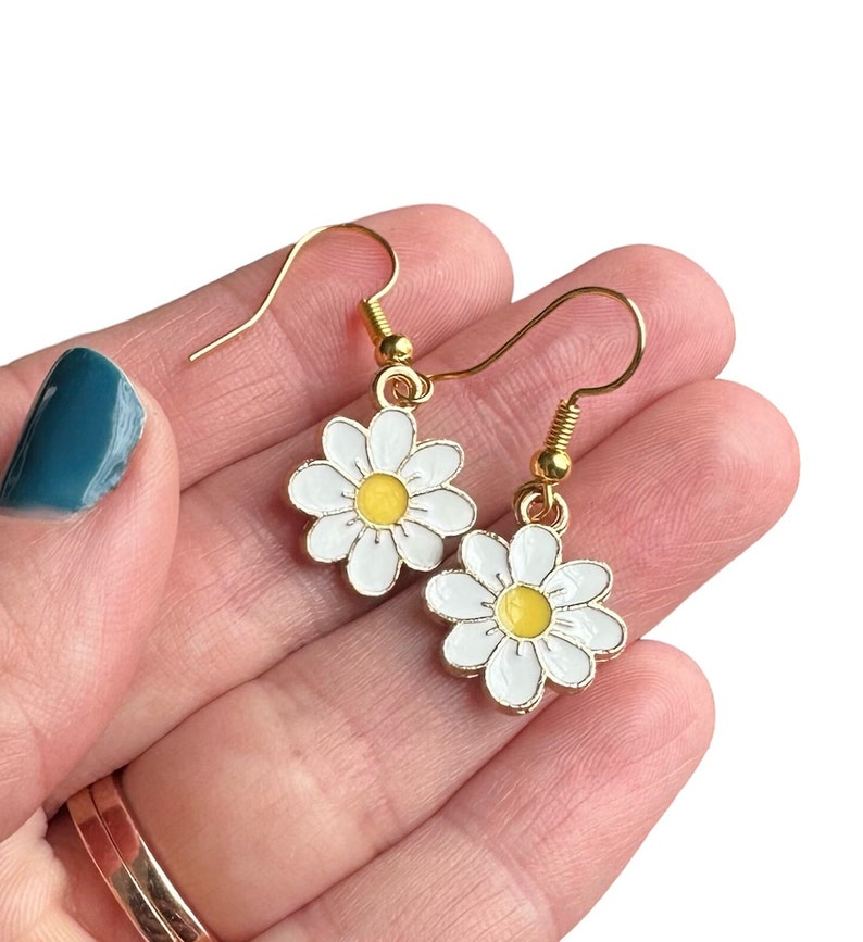 Small white daisy flower earrings with yellow centers, dangling from gold earring hooks.