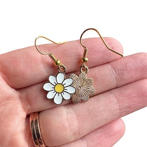 Front and back of daisy earrings dangling from gold earring hooks.