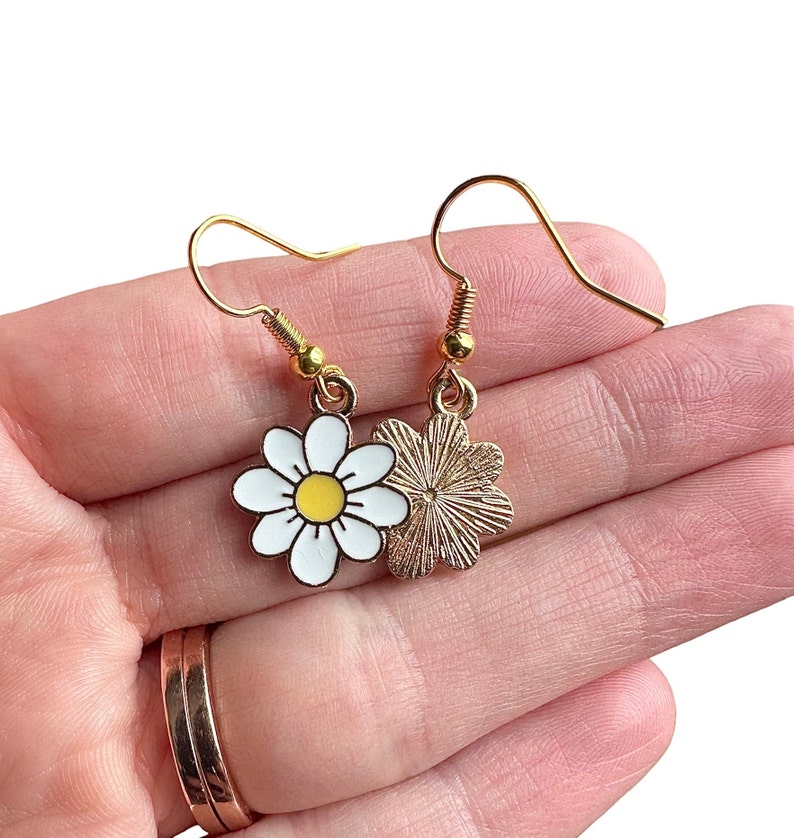 Front and back of daisy earrings dangling from gold earring hooks.