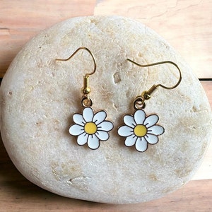 Small, dainty white daisy flower earrings with yellow centers, dangling from gold earring hooks.