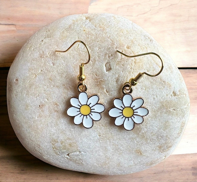 Small, dainty white daisy flower earrings with yellow centers, dangling from gold earring hooks.