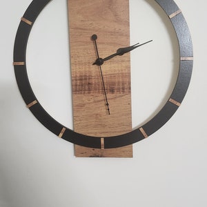 Puede incluir: Un reloj redondo negro con detalles dorados y un marco de madera. Las manecillas del reloj son negras y apuntan a la hora.