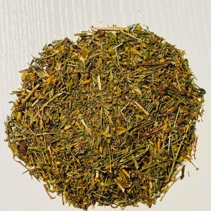 May include: A close-up of a pile of dried herbs and flowers, displaying a mix of green, yellow, and brown colours. The texture is coarse and natural, indicating a blend of various plant parts. The image is taken from above.