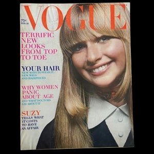 以下が含まれることがあります： ブロンドの髪と前髪を持つ笑顔の女性が特徴の、ヴィンテージのVogueマガジンの表紙。表紙にはオレンジ色のVogueのロゴがあり、「Terrific New Looks From Top To Toe」や「Your Hair」などのピンクと白のテキストがあります。