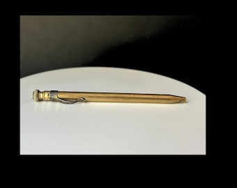 May include: A vintage brass mechanical pencil with a silver clip and a textured end. The pencil is lying on a white surface, with a dark background. The pencil is approximately 5.5 inches long.