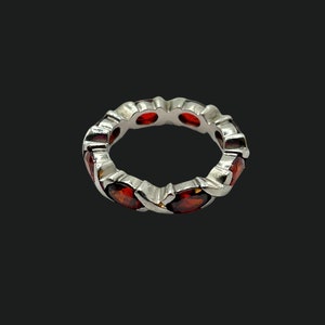 May include: A silver ring with a continuous pattern of oval-shaped, deep red gemstones. The gemstones are set closely together, creating a full band of color. The ring is displayed against a dark background.