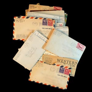 May include: A pile of vintage airmail envelopes and postcards, with red, white, and blue striped borders. Some envelopes have postage stamps and postmarks, with the words "VIA AIR MAIL" visible. The background is black.