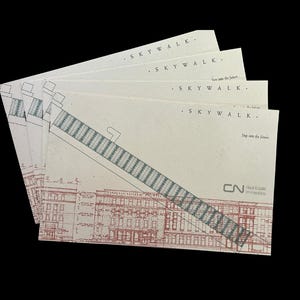May include: A stack of cream-colored postcards with architectural drawings. The cards feature the word "SKYWALK" and the phrase "Step into the future." A detailed illustration of a building and a skywalk is visible.
