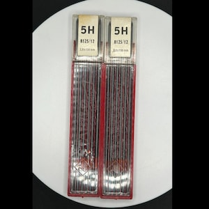 May include: Two rectangular pencil lead containers. Each container has a clear plastic front and a red plastic frame. The labels read "5H" and "8125/12". The lead is 2.0 x 130 mm.